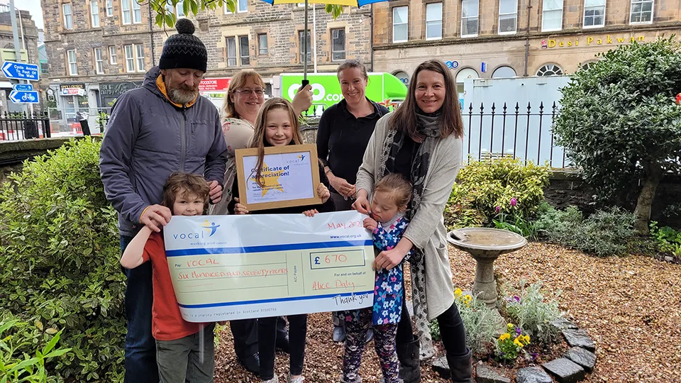 Alice holding certificate and cheque for the £670 she raised for Vocal, surrounded by her family and some Vocal staff.