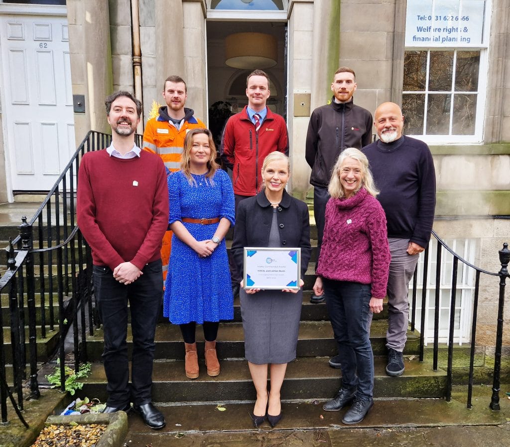 4 senior staff at Vocal and 4 from Lothian Buses, standing in front of our Edinburgh Carers' Hub, proudly holding the commendation certificate from the Edinburgh Chamber of Commerce awards.