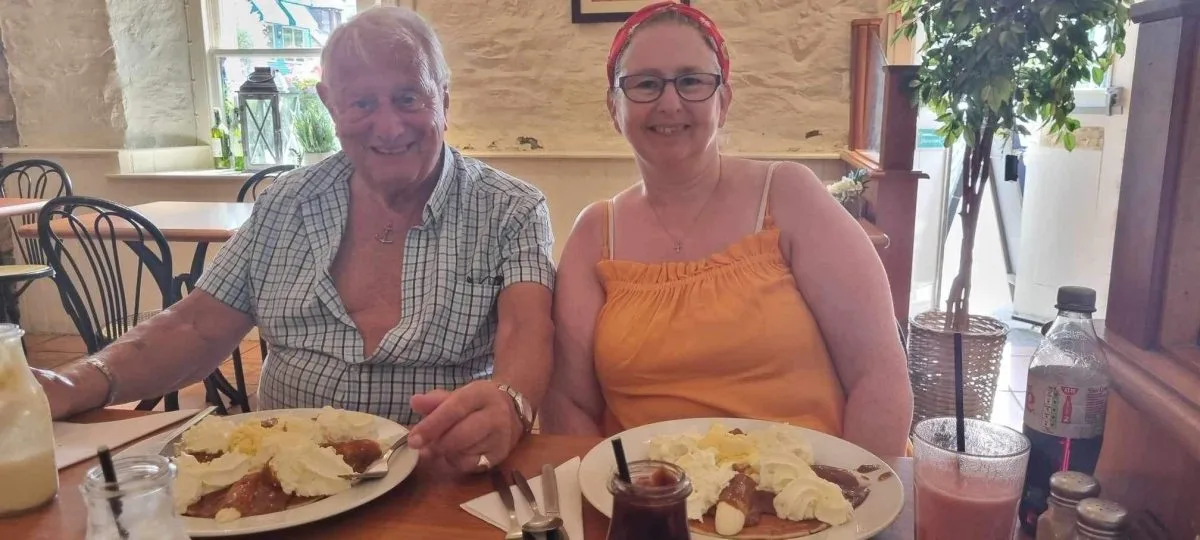 Kirsty, a carer and reception volunteer at our Edinburgh Carers' Hub, sits in a cafe with her dad. They are both smiling at the camera and about to eat pancakes.