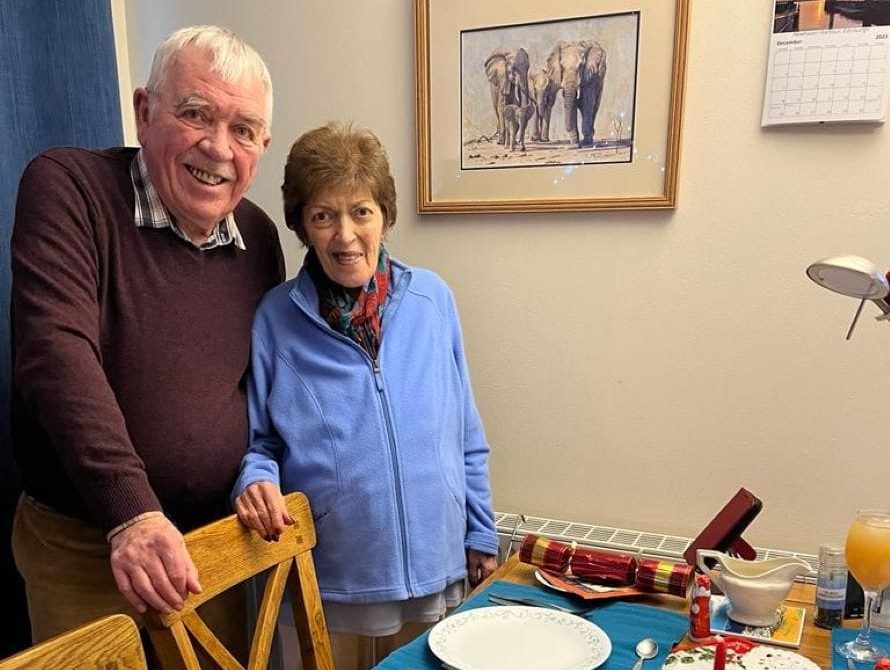 Stan and Anne standing at the dining table, about to sit down for Christmas dinner.