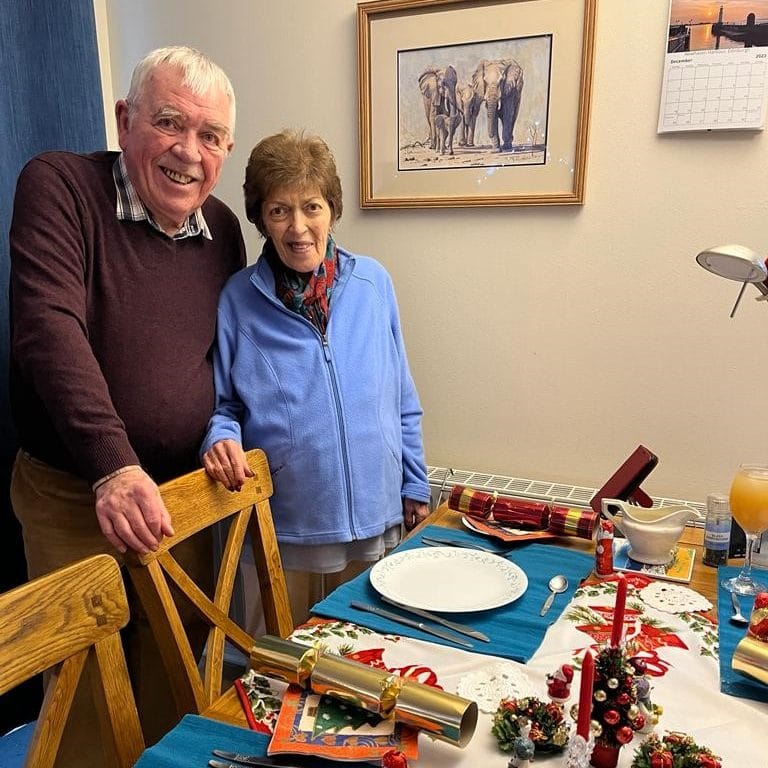 Stan and Anne standing at the dining table, about to sit down for Christmas dinner.