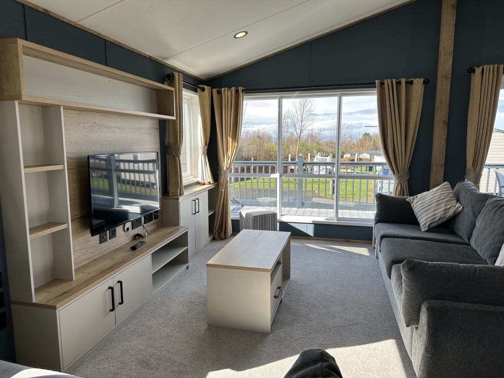 Living room area in Seton Sands holiday home, with big sofa, big window, TV and coffee table.