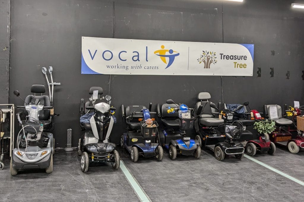 A selection of motorised wheelchairs, scooters and walking aids displayed in Treasure Tree's new unit in Ocean Terminal. The sign on the wall has logos for Vocal and Treasure Tree.